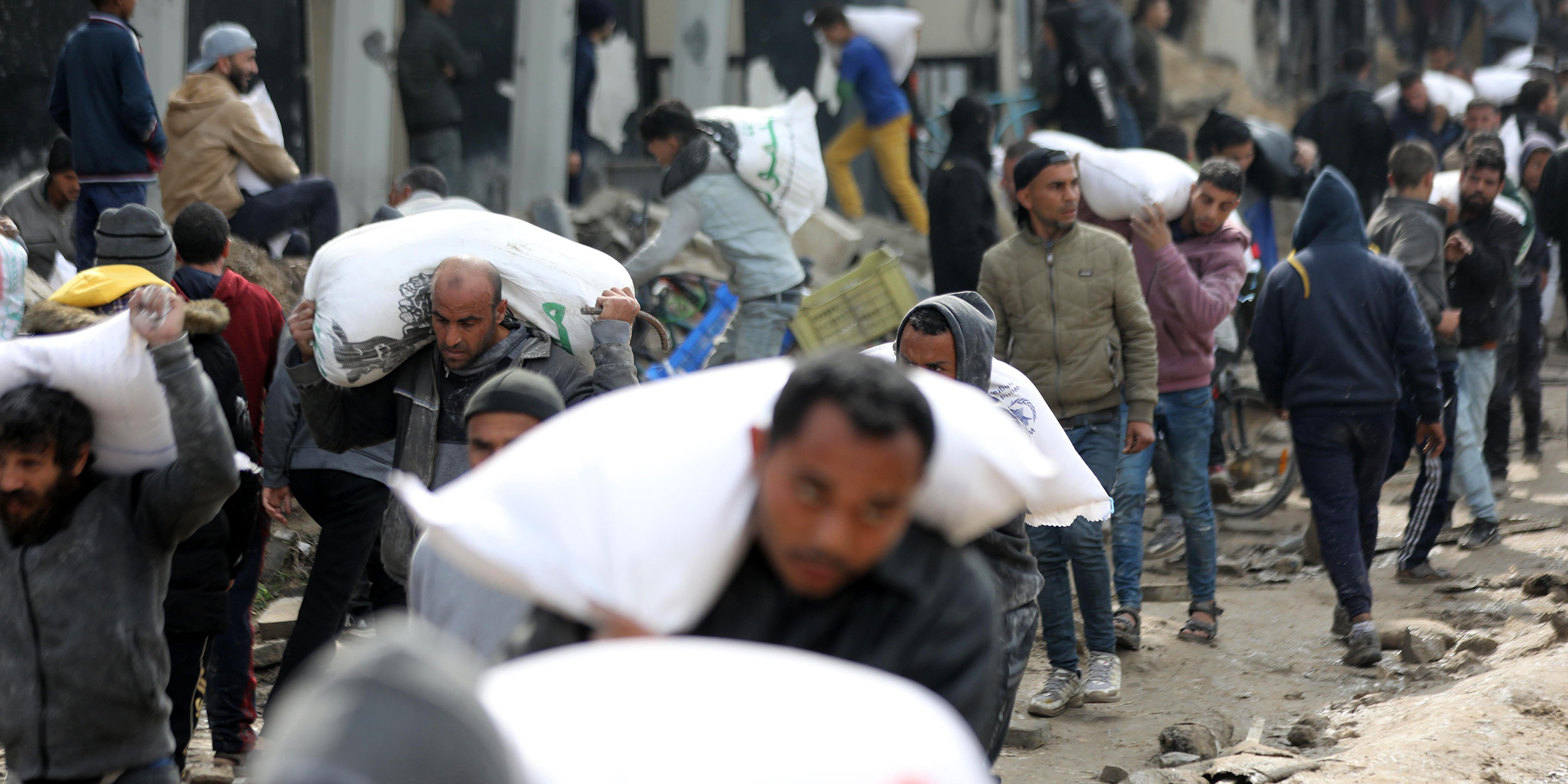 GAZA CITY, GAZA - FEBRUARY 19: Palestinians receive bags of flour as they wait for aid supplies carried by trucks to enter from the border in Gaza Strip on February 19, 2024. The Israeli war on Gaza has pushed 85% of the territory's population into internal displacement amid acute shortages of food, clean water, and medicine, while 60% of the enclave's infrastructure has been damaged or destroyed, according to the UN. (Photo by Dawoud Abo Alkas/Anadolu via Getty Images)