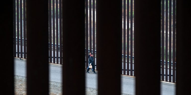 Migrants and asylum seekers walk to be processed by the Border Patrol between fences at the US-Mexico border seen from Tijuana, Baja California state, Mexico, on June 5, 2024. President Joe Biden said Tuesday he had ordered sweeping new migrant curbs to "gain control" of the US-Mexico border, making a dramatic bid to neutralize one of his political weak spots in his reelection battle against Donald Trump. (Photo by Guillermo Arias / AFP) (Photo by GUILLERMO ARIAS/AFP via Getty Images)